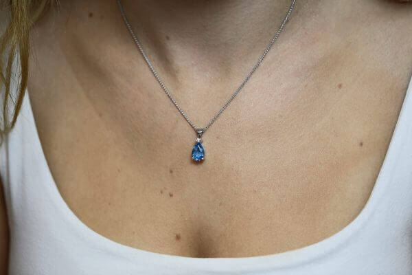 A woman wearing a Pear Shape Topaz and Diamond Pendant C786 necklace with a blue topaz tear.