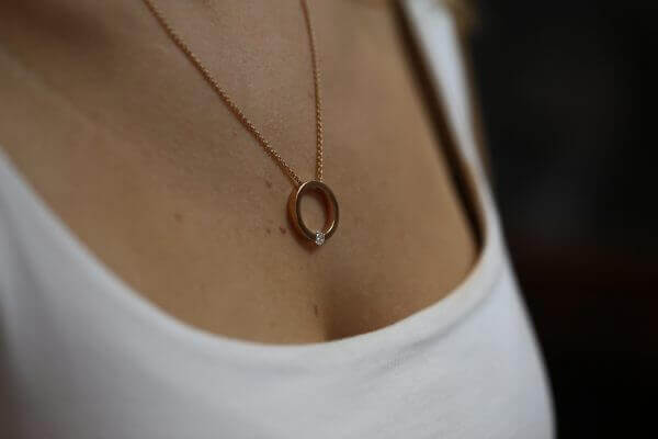 A close up of a woman's neck with a gold circle necklace and a Tension set diamond necklace C1061-RG.