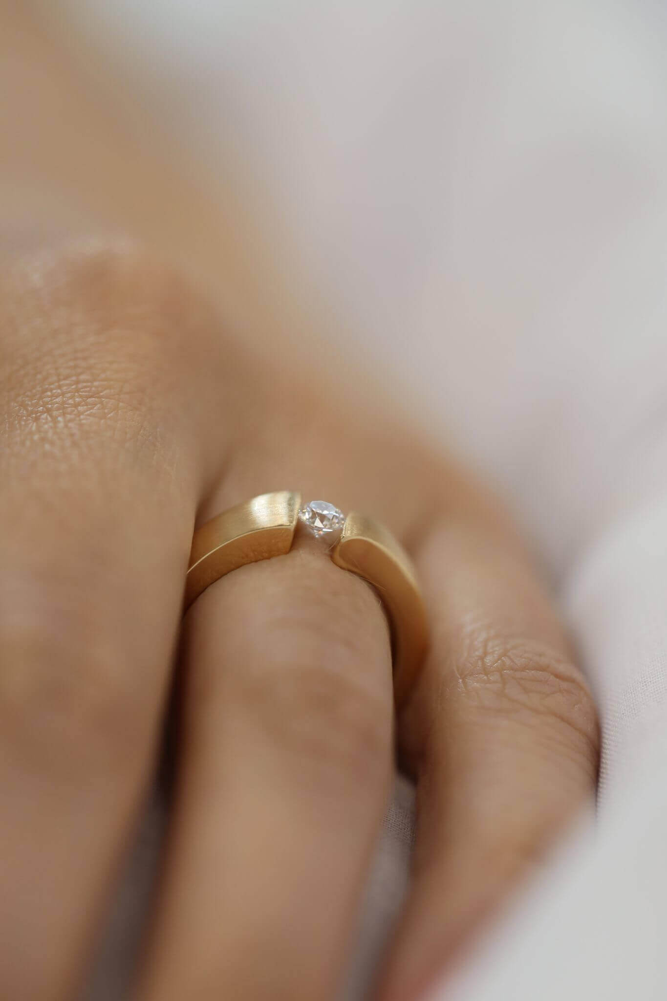 A woman wearing a Yellow Gold Flat Tension Set Round Diamond Ring C745 with a round diamond.