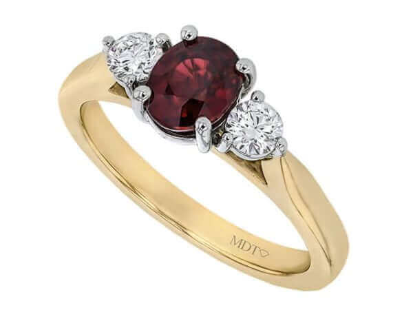 Gold ring with red gemstone flanked by diamonds.